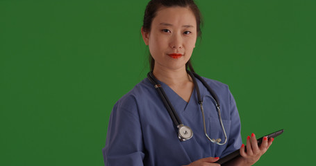 Female Asian medical doctor posing with portable tablet computer on green screen