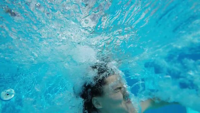 An original view of a young woman jumping in the pool and shot underwater. She sends many bubbles up, looks frightened and funny in slo-mo