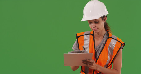 Female construction worker writing notes on clipboard on green screen