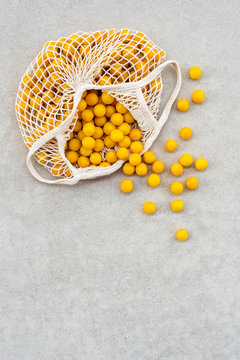 Yellow plums in a mesh bag on concrete background