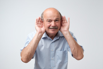 Portrait of senior casual man which overhears conversation over white background. Speak loudly please concept.