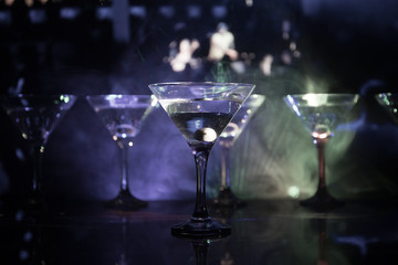 Several glasses of famous cocktail Martini, shot at a bar with dark toned foggy background and disco lights. Club drink concept