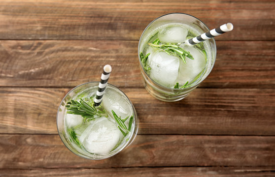 Glasses of refreshing cucumber cocktail with rosemary on wooden table, top view