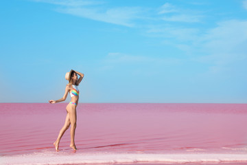 Beautiful woman in swimsuit standing near pink lake on sunny day