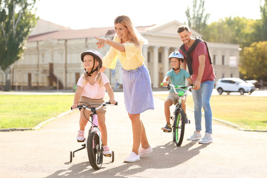 Happy parents teaching children to ride bicycles outdoors