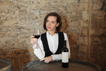 Fototapeta na wymiar Female sommelier with glass of red wine at table indoors