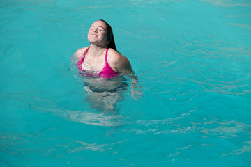 Woman comes up for air after jumping into a swimming pool. Young brunette woman in pink bikini coming up out of the water in an outdoor swimming pool.