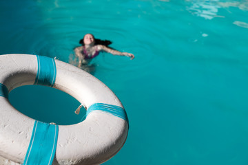 Man holding a blue and white life saver out to help save a drowning woman in a swimming pool. Lifeguard holding life preserver out to a person in distress in an outdoor swimming pool.