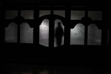 Silhouette of an unknown shadow figure on a door through a closed glass door. The silhouette of a human in front of a window at night. Scary scene halloween concept of blurred silhouette