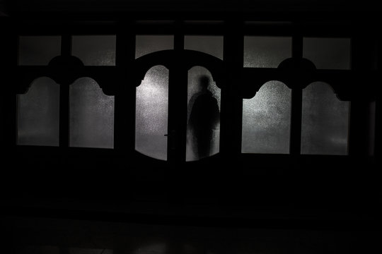 Silhouette of an unknown shadow figure on a door through a closed glass door. The silhouette of a human in front of a window at night. Scary scene halloween concept of blurred silhouette