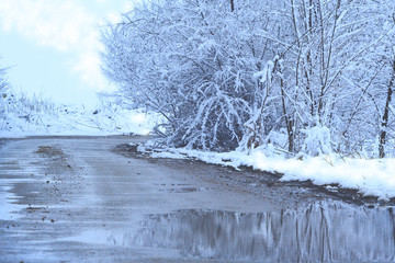 the first snow in autumn on the road in the forest melts in the rays of the warm sun creating puddles and mud