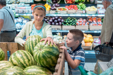 Girl in a grocery store checking a watermelon for quality.