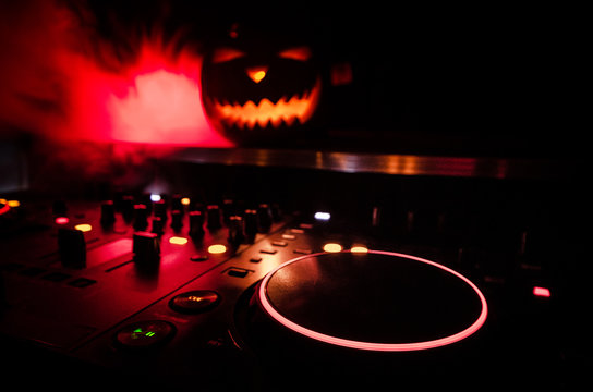 Halloween pumpkin on a dj table with headphones on dark background with copy space. Happy Halloween festival decorations and music concept. Toned