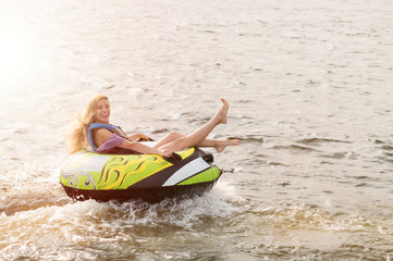 A beautiful young girl is floating on an inflatable circle tied to a boat