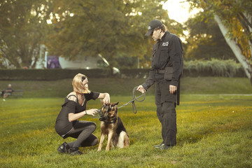 Naklejka na ściany i meble Policeman in uniform reproaching lady with german shepherd in city park