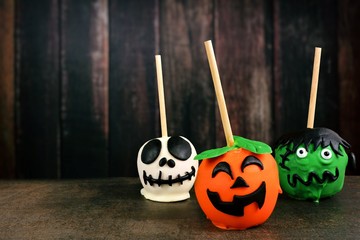 Three unique Halloween candy apples against a dark wood background. Skeleton, jack o lantern and monster.
