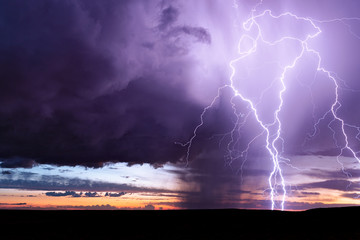 Lightning bolts strike from a sunset storm.