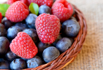 Freshly picked organic raspberries and blueberries in a basket on a burlap cloth background.Blueberry and raspberry. Healthy eating,summer fruits or diet concept.Selective focus.