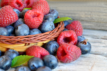 Freshly picked organic raspberries and blueberries in a basket on old wooden background.Blueberry and raspberry. Healthy eating,summer fruits or diet concept.Selective focus.