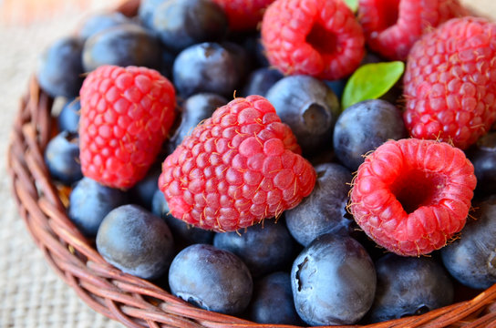 Freshly picked organic raspberries and blueberries in a basket on a burlap cloth background.Blueberry and raspberry. Healthy eating,summer fruits or diet concept.Selective focus.