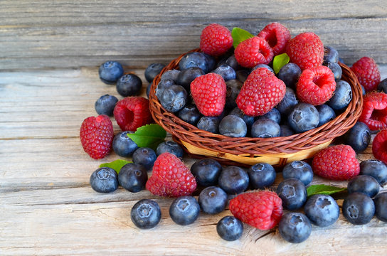 Freshly picked organic raspberries and blueberries in a basket on old wooden background.Blueberry and raspberry. Healthy eating,summer fruits or diet concept.Selective focus.