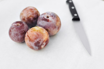 A knife beside four honey punch pluot fruits on white wax paper