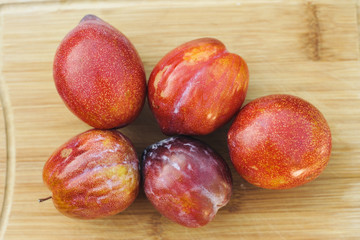 A group of 5 amigo pluot fruits with a knife on a wood cutting board