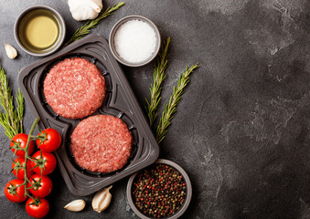 Obraz na płótnie Canvas Plastic tray with raw minced homemade beef burgers with spices and herbs. Top view with space for text.On kitchen table background with tomatoes salt and pepper.