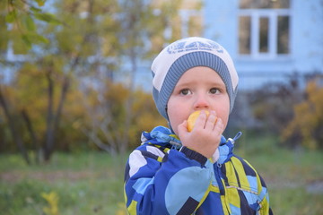 A little boy eating an apple on the street.