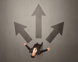Young contemplating businessman stands in front of brown arrows