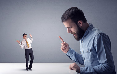 Young professional businessman being angry with an other miniature businessman in front of a grey...