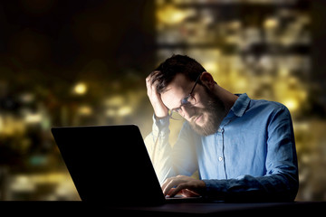 Young handsome businessman working late at night in the office with city lights in the background
