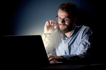 Young handsome businessman working late at night in the office with a dark background