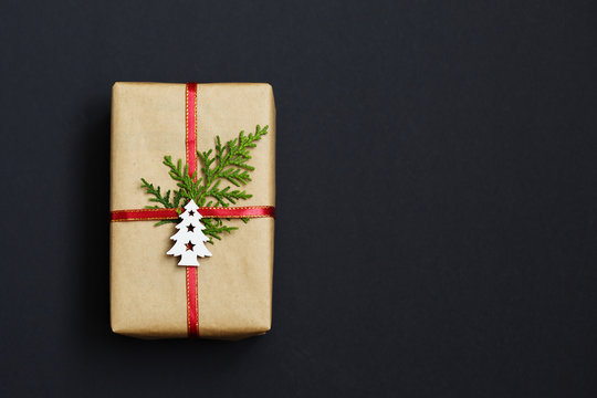 Christmas handmade gift box decorated with craft paper and white Christmas tree on dark background top view. Merry christmas greeting card. Happy New