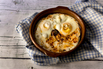 Fried eggs in clay pot on a white wooden background