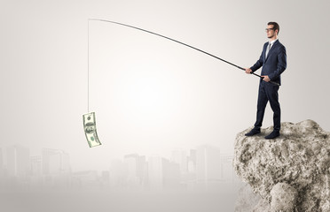 Elegant young businessman fishing cash from a huge rock