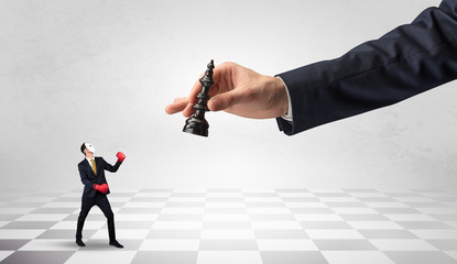 Fototapeta premium Small businessman fighting against big chessman on a big hand with chess board concept 