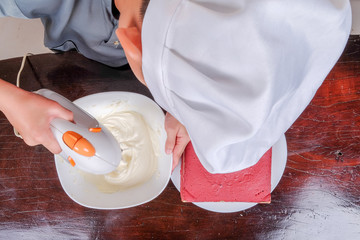 Top view of Happy  boy making whipped cream in glass bowl and preparing a red velvet cake.