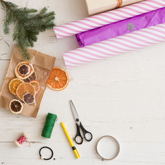 Top view on Christmas gifts and decorations: paper, tree branch and ribbons on wooden table.