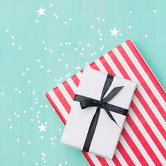 Obraz premium Closeup of beautiful Christmas gifts wrapped in white and striped gift paper decorated with ribbon and sparkling stars on turquoise wooden table. New Year, holidays and celebration concept