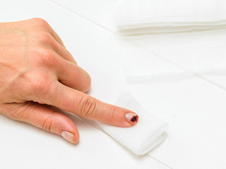 Wounded index finger of a woman's hand and dressing material on a white table.