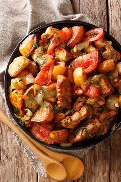 Ojahuri fried meat with potatoes, tomatoes, herbs and spices close-up on a frying pan. Vertical top view