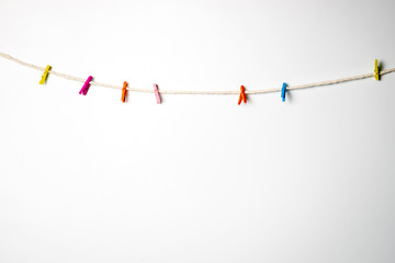 Multi Color wooden clip hanging with white rope with white background.