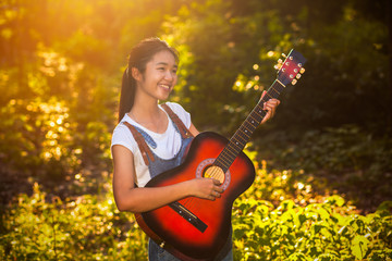 Women playing guitar in the woods on a sunny day.
