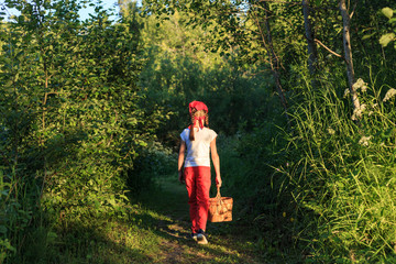 Young girl walking on a path through green woods carrying a birchbark basket