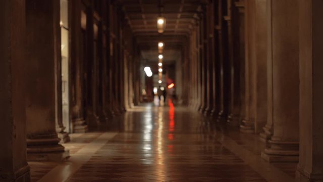 Hallway lined up with columns in the ancient building on St. Marks Square. Dim light, people walking in the distance
