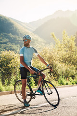 Fototapeta premium A man with a bicycle in the mountains. Road in the mountains covered with forest.