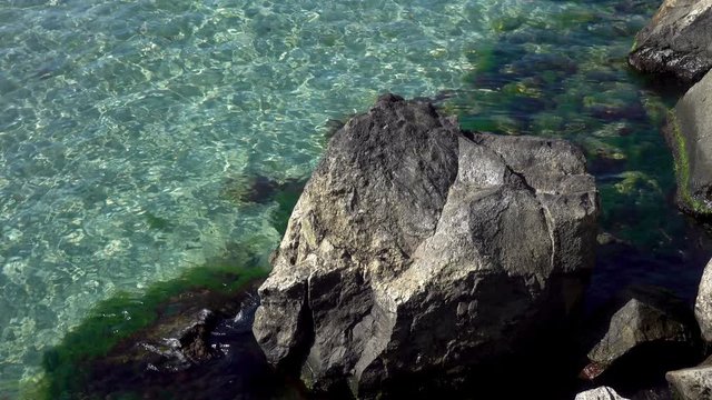 4K view of clear sea water near a rocky shore.