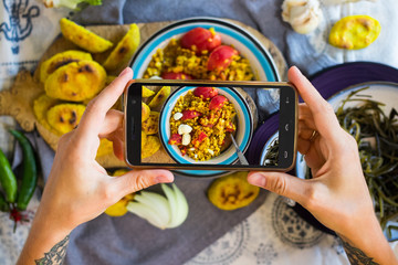 Woman hands takes photography of food on table with phone. Dinner, lunch. Indian curry lentil with tomatoes. Smartphone photo for social networks or blogging post. Vegetarian, healthy, organic © Viktor Kochetkov