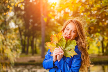 Naklejka na ściany i meble Cute smiley woman holding autumn leafs in the nature.